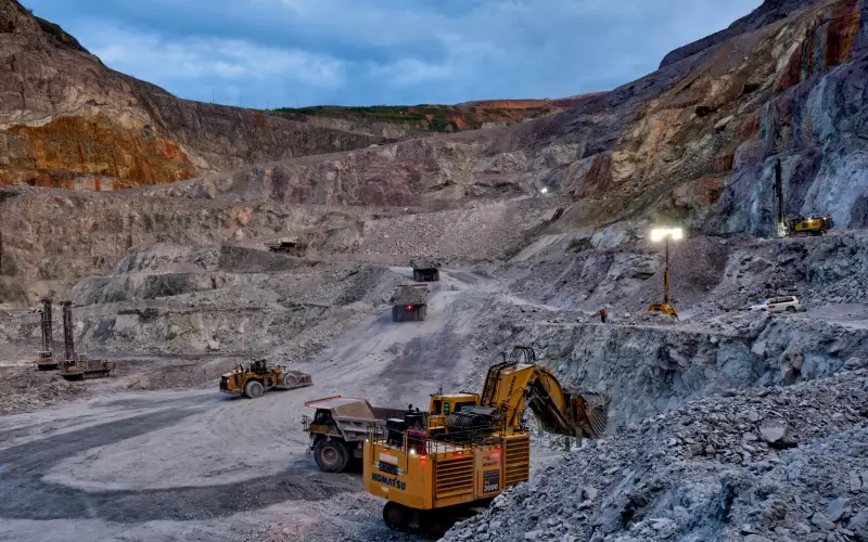 An open-pit mining site with heavy excavators and haul trucks, illustrating the application of wear-resistant studs on industrial machinery components.