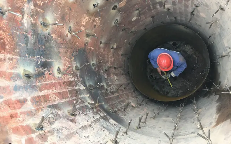 A worker installing Y-shaped refractory anchors inside an industrial kiln to secure refractory lining materials.