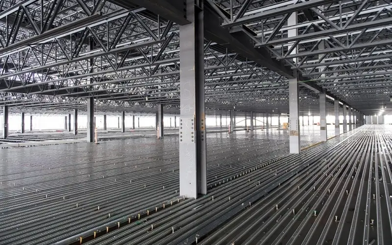 Interior of an industrial warehouse under construction with steel truss roof and steel decking floor
